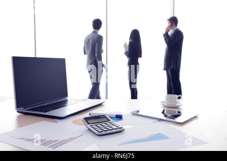 Documenti finanziari , laptop, calcolatrice sulla tavola , business team sullo sfondo Foto Stock