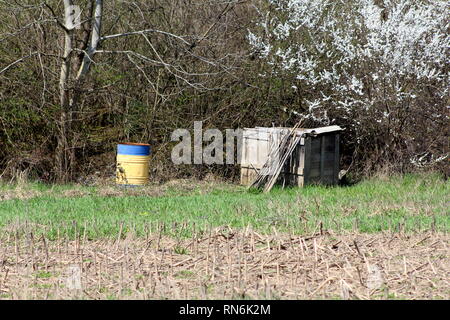Cilindretto metallico utilizzato per lo stoccaggio di acqua piovana accanto alle improvvisate scatola di legno usato come palo di composto circondato da erba non tagliata e raccolte cornfield Foto Stock
