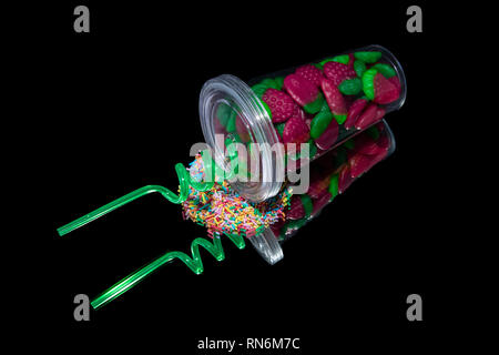 Colorate fragole gommoso in un vetro-shake con paglia e multicolori pepite di zucchero su uno specchio e uno sfondo nero Foto Stock