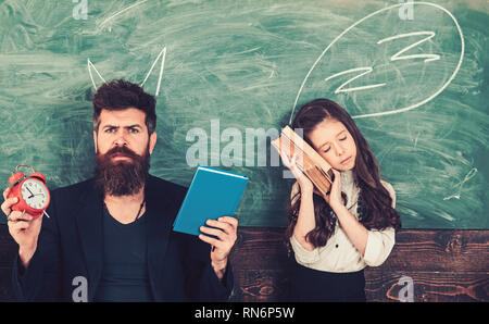 Tempo per apprendere il concetto. Insegnante devil e sleepy ragazza. Uomo Barbuto con sveglia e prenota. Bambino studente stanco di studio nella scuola. Tutor e Foto Stock