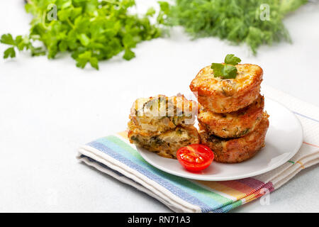 Una sana prima colazione. broccoli morsi di formaggio (Muffin), pomodori freschi, erbe fresche sul calcestruzzo leggero sottofondo. snack per dieta cheto Foto Stock