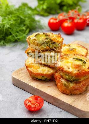 Una sana prima colazione. broccoli morsi di formaggio (Muffin), pomodori freschi, erbe fresche sul calcestruzzo leggero sottofondo. snack per dieta cheto Foto Stock