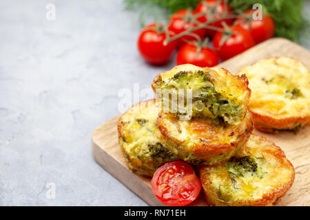 Una sana prima colazione. broccoli morsi di formaggio (Muffin), pomodori freschi, erbe fresche sul calcestruzzo leggero sottofondo. snack per dieta cheto Foto Stock