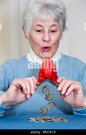 Immagine composita di un facoltoso senior donna anziana con espressioni di sorpresa lo svuotamento di un mucchio di denaro al di fuori di un portamonete. Inghilterra Regno Unito Gran Bretagna Foto Stock