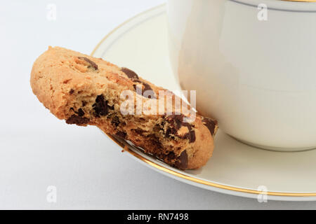 Tazza di tè inglese su un piattino e un chip di cioccolato biscotto con un morso prelevato. Inghilterra Regno Unito Gran Bretagna Foto Stock