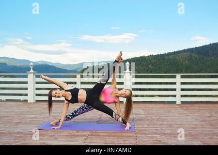 Attività sportive e donne flessibile stretching, bilanciamento sul materassino yoga. Due ragazze facendo esercizi e yoga all'aperto all'aria fresca. Donna sorridente, indossa nel quartiere alla moda di abbigliamento sportivo. Foto Stock