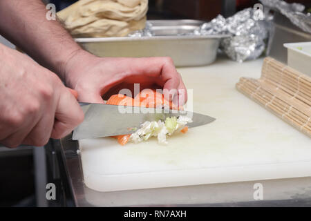 Primo piano della mano è il cuoco che taglia un rotolo di Philadelphia in un ristorante di cucina con un coltello affilato di sushi. Concetto di cucina piatti Giapponesi Foto Stock