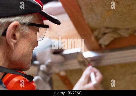 Uomo in googles facendo un segno sul telaio di metallo su attico incompiuto soffitto. Attico isolamento e rinnovo Foto Stock