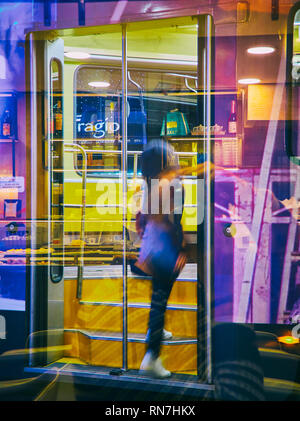 Una giovane donna anonima prendendo un tram a Milano Centro a notte. Lombardia, Italia. Vista attraverso il riflesso della vetrina di un bar. Foto Stock