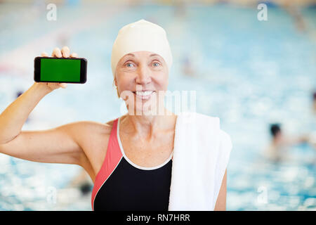 Senior donna presentando lo smartphone nel pool Foto Stock