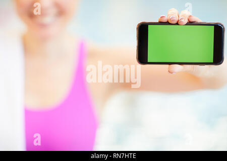 Donna presentando lo smartphone nel pool Foto Stock