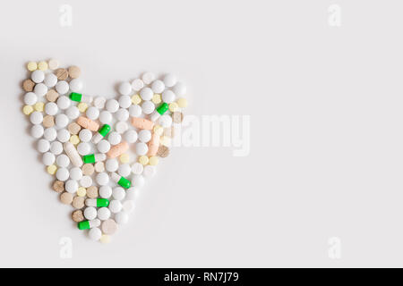 Concetto di medicina bianco, verde e arancione vitamine e compresse. Cuore da pillole colorate a isolato sullo sfondo bianco. Vista da sopra con copia spazio, fl Foto Stock