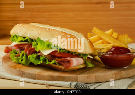 Sommergibile freschi sandwich con formaggio, pancetta, pomodori e lattuga, sulla luce sullo sfondo di legno Foto Stock