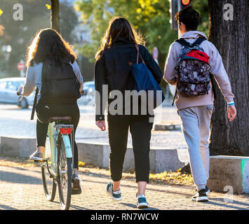 Strasburgo, Alsazia, Francia, Europa, vista posteriore di 2 adolescenti a piedi e una ragazza in bicicletta sul marciapiede, Foto Stock