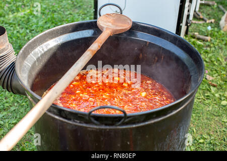 La preparazione di piatti tradizionali ungheresi zuppa di gulasch bograch in una grande pentola di metallo calderone sul fuoco del gas Foto Stock