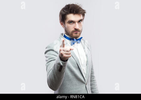 Ritratto di grave bossy bello uomo barbuto in casuale completo grigio e blu bow tie in piedi, guardando la fotocamera e riscaldamento. piscina studio shot, isola Foto Stock