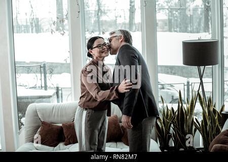 Tall grey-haired uomo bello in una maglietta blu sussurra qualcosa all'orecchio womans Foto Stock