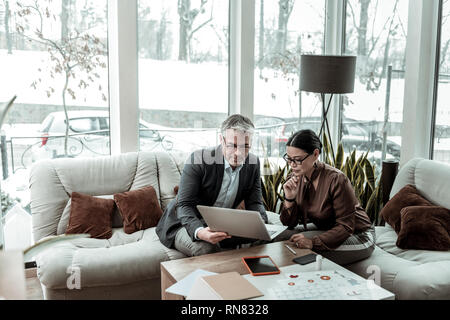 Tall grey-haired uomo bello in una camicia scura e il suo partner cercando coinvolti Foto Stock