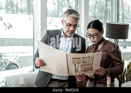 Tall grey-haired uomo bello in una camicia scura e il suo partner analizzando il progetto Foto Stock