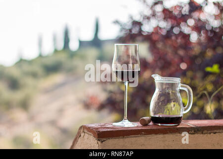 Sorseggiate un bicchiere di vino rosso di Toscana, Italia. Sfocata vigneti in background. Foto Stock
