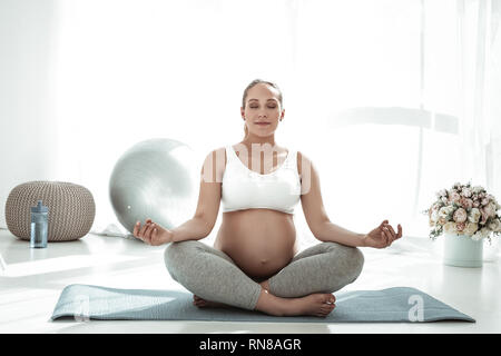 Calma e tranquilla donna incinta seduta nella postura meditativa Foto Stock