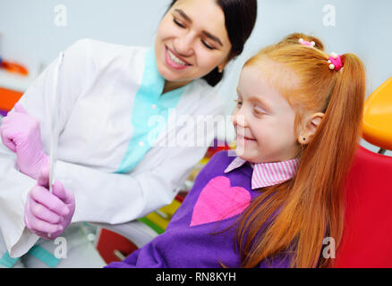 Bambini il dentista esamina i denti e la bocca del bambino - un simpatico i Capelli rossi ragazza seduta in una poltrona odontoiatrica Foto Stock