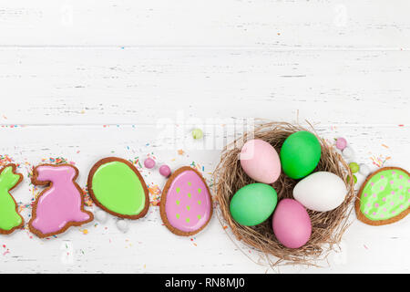 Pasqua biglietto di auguri con colorati gingerbread cookie e uova di pasqua nel nido. Vista dall'alto sul tavolo di legno con lo spazio per i messaggi di saluto Foto Stock