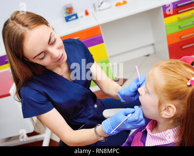 Bambini il dentista esamina i denti e la bocca del bambino - un simpatico i Capelli rossi ragazza seduta in una poltrona odontoiatrica Foto Stock