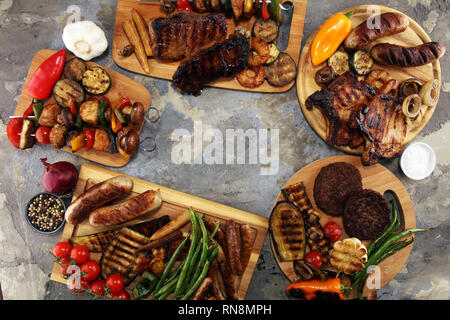 Un assortimento di deliziose grigliate di carne con verdure ed erbe sul tavolo rustico Foto Stock