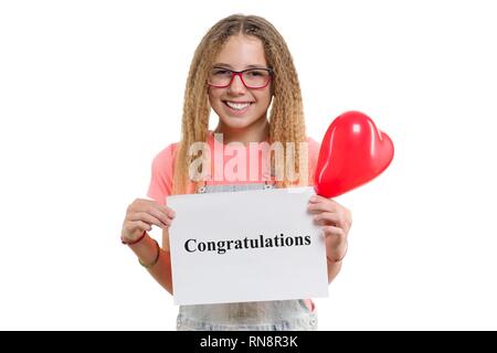 Congratulazioni messaggio di testo scritto sul libro bianco in mani piuttosto giovani teen ragazza sorridente ragazza con cuore rosso palloncino isolato su sfondo bianco. Foto Stock