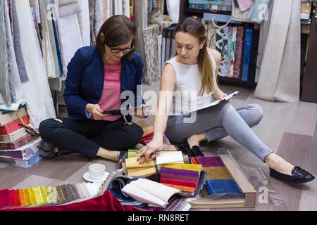 Le donne guarda i campioni di tessuti per tende e rivestimenti di mobili in una nuova casa Foto Stock