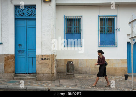 Donna locale oltrepassando palazzo coloniale con blu brillante di windows. La Candelaria, il quartiere storico di Bogotà, Colombia. Sep 2018 Foto Stock