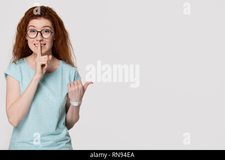 I Capelli rossi ragazza con il dito sulle labbra per tenerlo tranquillo Foto Stock