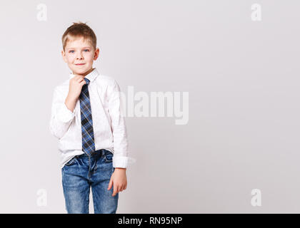 Grazioso piccolo ragazzo sorridente in una camicia bianca e in un elegante cravatta in posa su una luce di sfondo grigio. Ritratto di moda bambino maschio, muro grigio sul backgr Foto Stock