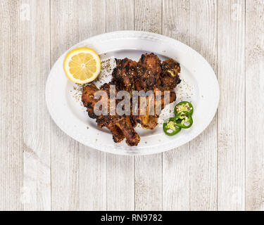Pollo arrosto bacchette con spezie indiane, limone e peperoncino jalapeno le fette su una piastra bianca. Foto Stock