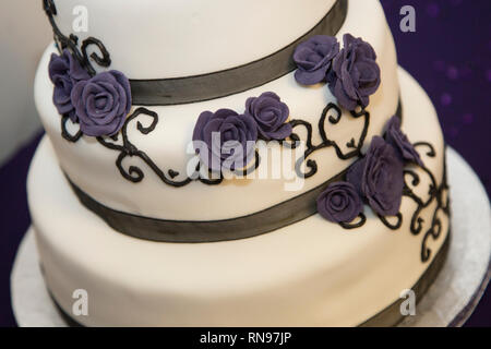 Close up il signor e la signora torta di nozze il giorno del matrimonio. Torta ha glassa bianca, viola nastro e zucchero a velo fiori viola decorare. Foto Stock
