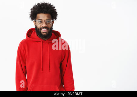 Vita-up shot di elegante urban americano africano freelancer maschio in felpa con cappuccio rosso e i bicchieri con gioia la sorridente e guardando la fotocamera con conchiglia e Foto Stock