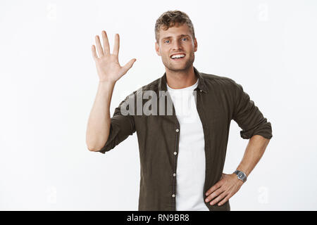 Atmosfera rilassata e spensierata amichevole maschile giovane atleta solleva palm come dando alta cinque o dire ciao, saluto con hi gesto e felice di nizza Foto Stock