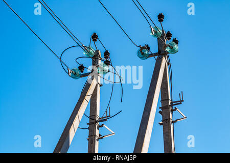 Pali in cemento con fili elettrici e ad alta tensione isolatori di distribuzione come parte di una linea di trasmissione contro un cielo blu. Foto Stock