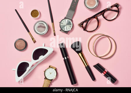 Vista dall'alto di orologi, rossetto, occhiali, occhiali da sole, ombretto, blush, spazzole cosmetiche, braccialetti e mascara Foto Stock