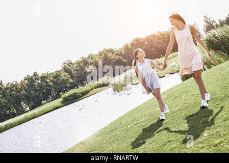 Genitore Single, madre e figlia camminando su un campo erboso tenendo le mani guardando ogni altra sorridendo felice Foto Stock