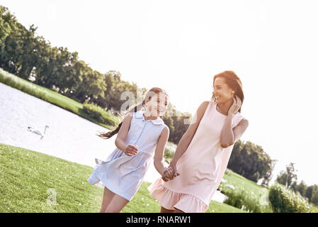 Genitore Single, madre e figlia camminando su un campo erboso tenendo le mani guardando ogni altro parlare sorridendo felice close-up Foto Stock