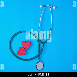 Verde stetoscopio medico e due rossi cuori di legno su sfondo blu Foto Stock