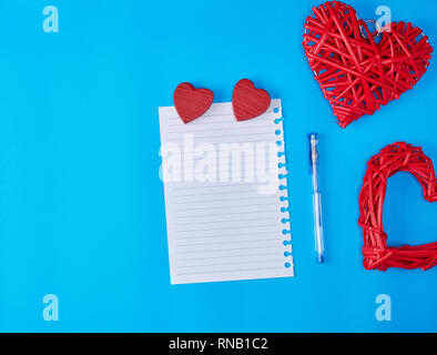 In vimini in legno cuore rosso e un vuoto di foglio bianco di notepad, sfondo blu Foto Stock