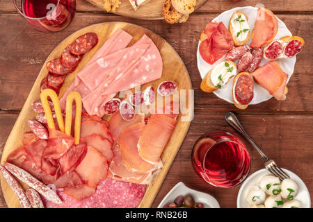 Salumi Gourmet. Molte diverse salsicce e prosciutti, salumi, girato dalla parte superiore al buio su un sfondo rustico con vino e panini Foto Stock