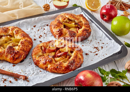 Aprire deliziose torte di mele, galette, con fette di mela ripieno su un vassoio da forno. apple, bastoncini di cannella, zucchero di canna e panno da cucina al backgrou Foto Stock