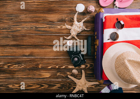 Vista superiore dell'estate accessori sulla valigia con retro telecamera cinematografica e conchiglie intorno su sfondo di legno Foto Stock