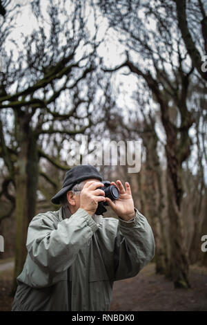 Uomo senior di dedicare il proprio tempo per il suo hobby preferito - fotografia - fotografie all'aperto con la sua fotocamera digitale/DSLR Foto Stock