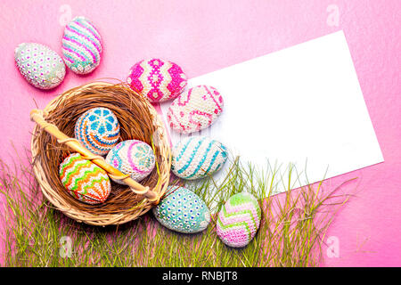 Colorate le uova di pasqua nel nido e di erba con vuoto carta bianca su sfondo rosa. Buona Pasqua Foto Stock