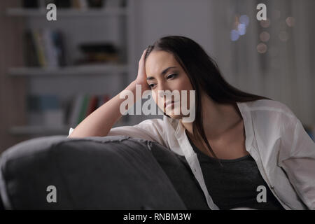 Triste donna guarda lontano seduto su un divano nella notte a casa Foto Stock